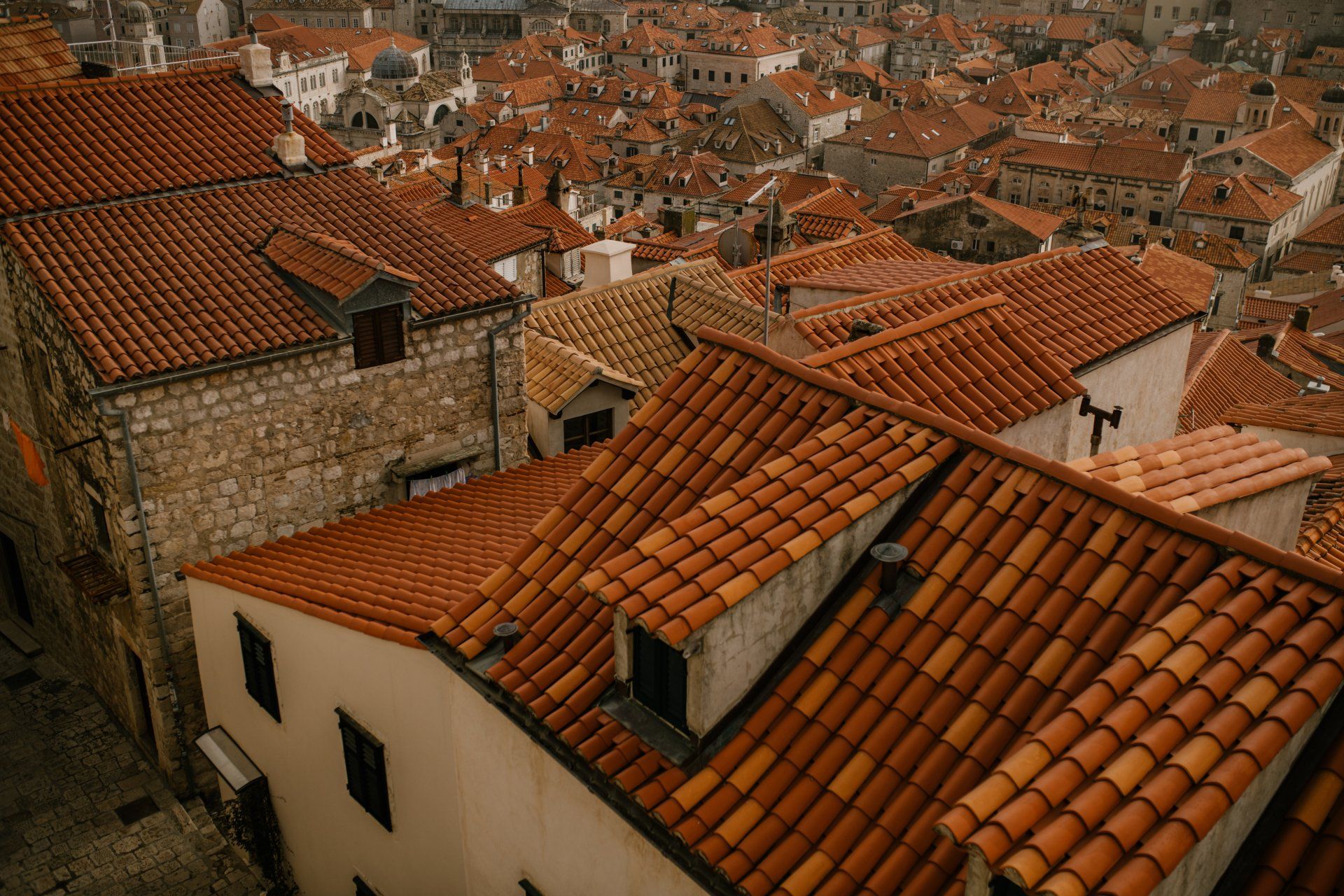 Vista elevada de numerosos tejados de tejas anaranjadas, con chimeneas, ventanas y edificios de piedra y fachadas claras.
